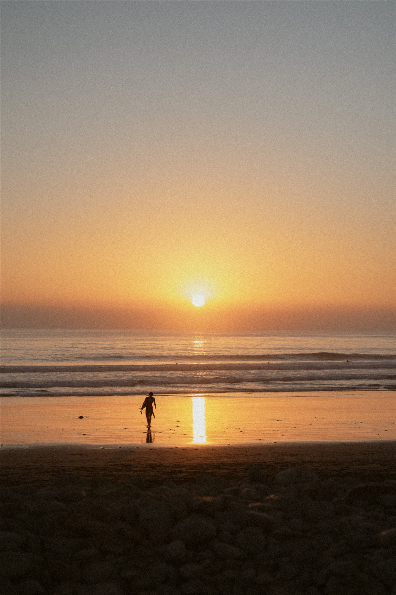 Surfer walking the beach at sunset with board under arm
